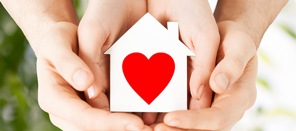 hands holding a toy house with a red heart painted on it